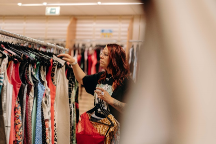 Dans un magasin de vêtements de seconde main, une femme s'occupe de l'agencement des vêtements tout en les examinant.